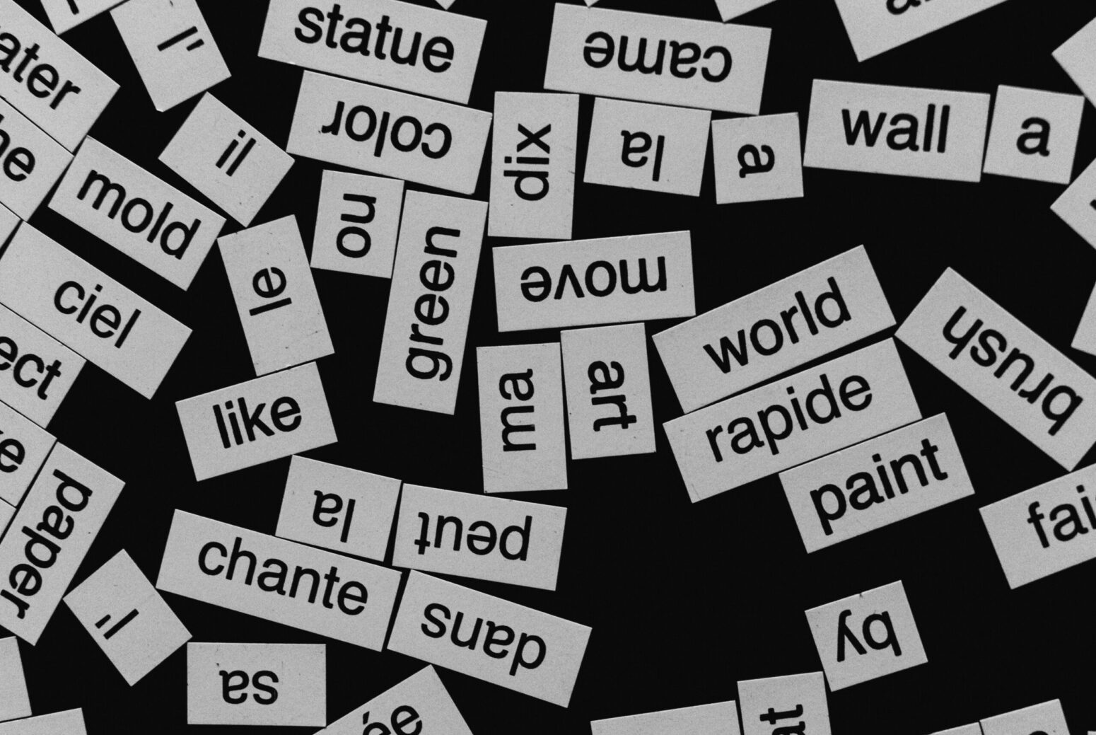 Paper cut-outs of various words scattered on a black background. Some of the words include "move," "world," "art," "chante," and "brush."
