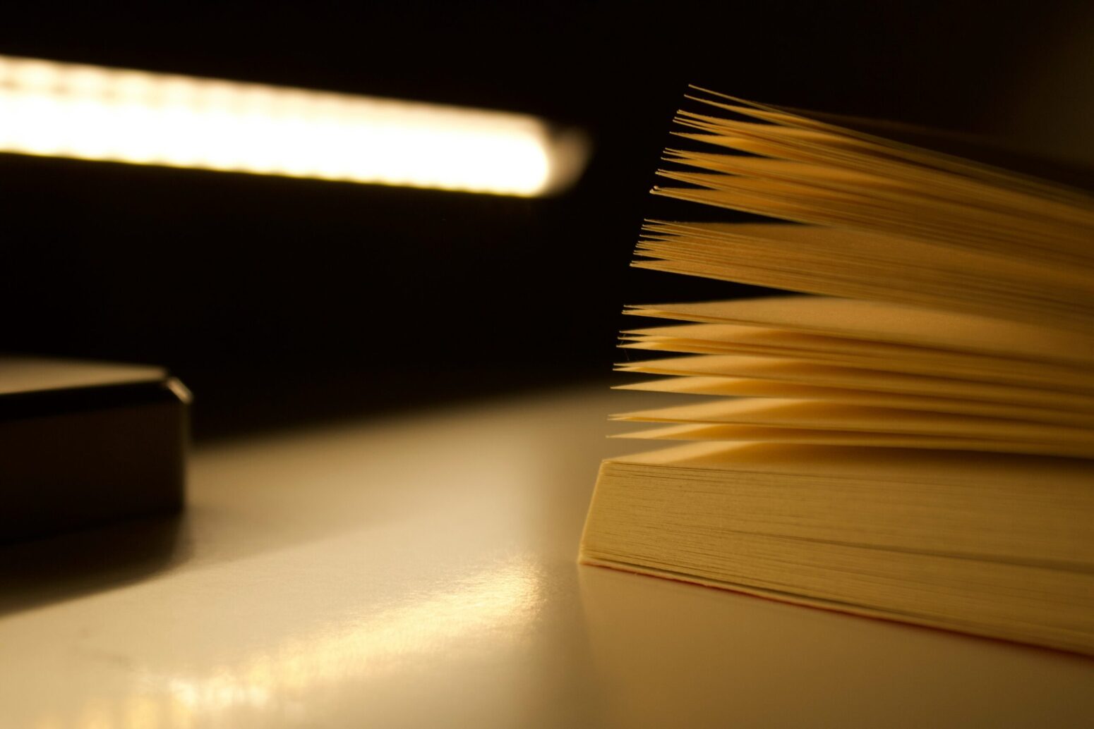 Close-up of the edge of an open book on a desk with a lamp. The pages are illuminated