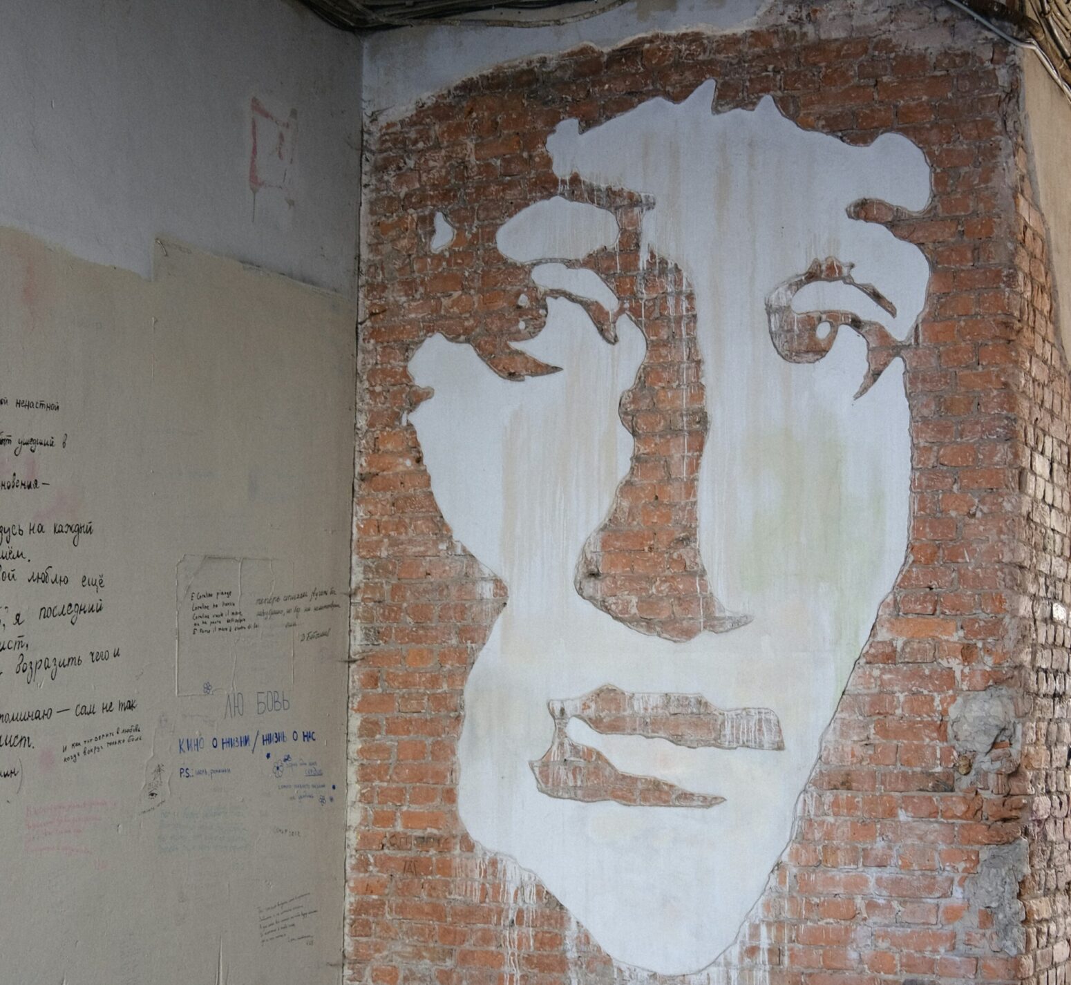 A mural of a woman (Anna Akhmatova) on an outside wall. There is handwriting on the conjoining wall