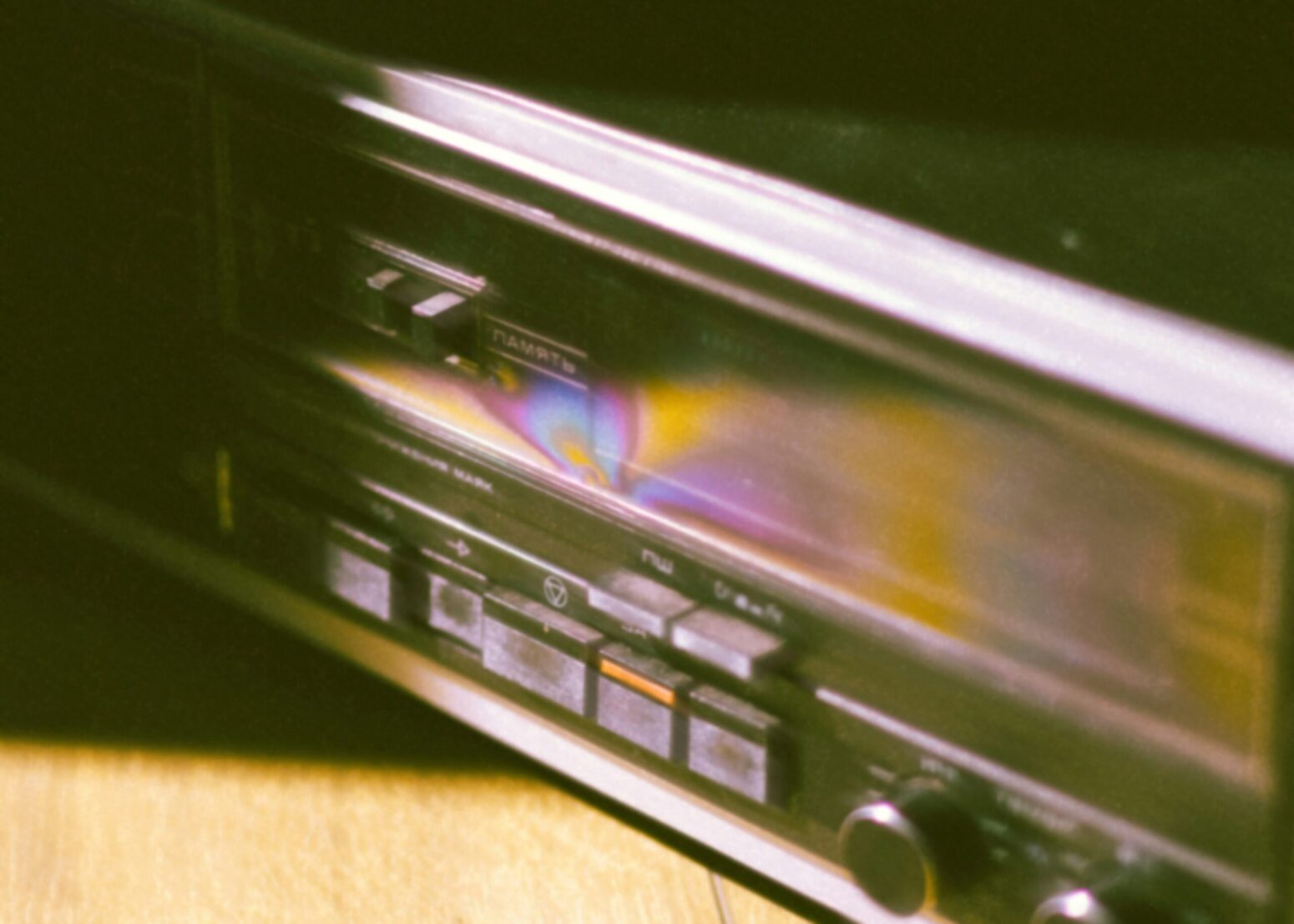 A fuzzy, close-up photo of a cassette player. It has black-and-silver buttons and dials, and it has a rainbow-like hue to it.