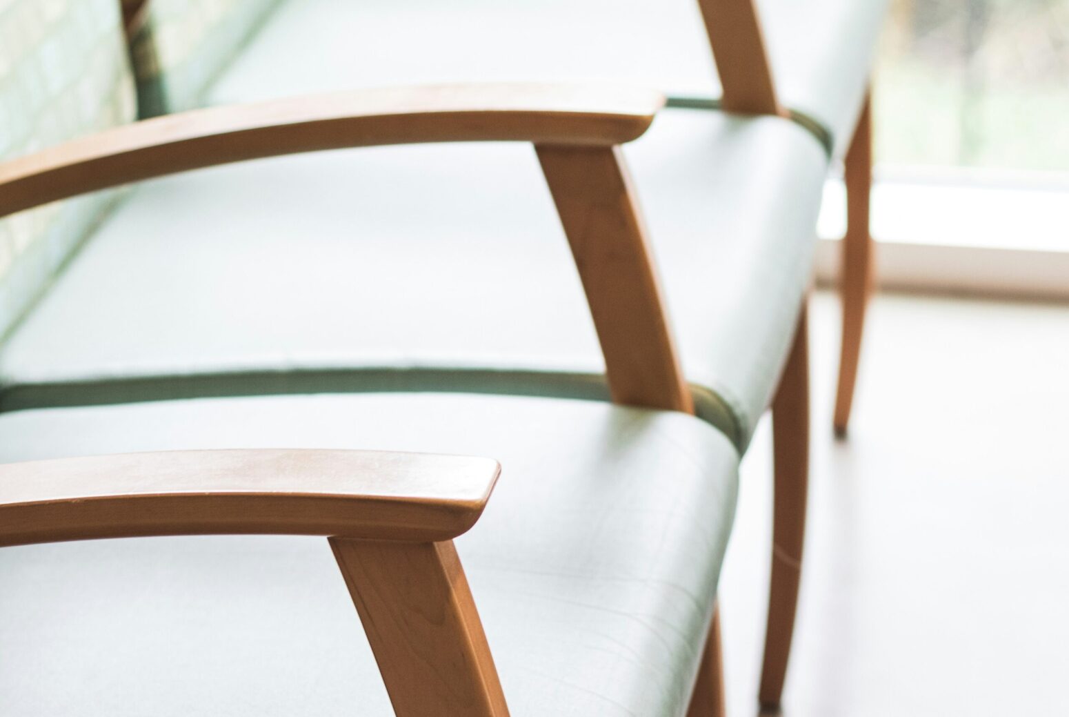 Three, green, vinyl-and-wooden chairs next to each other. They sit in a room with white floors and a window.