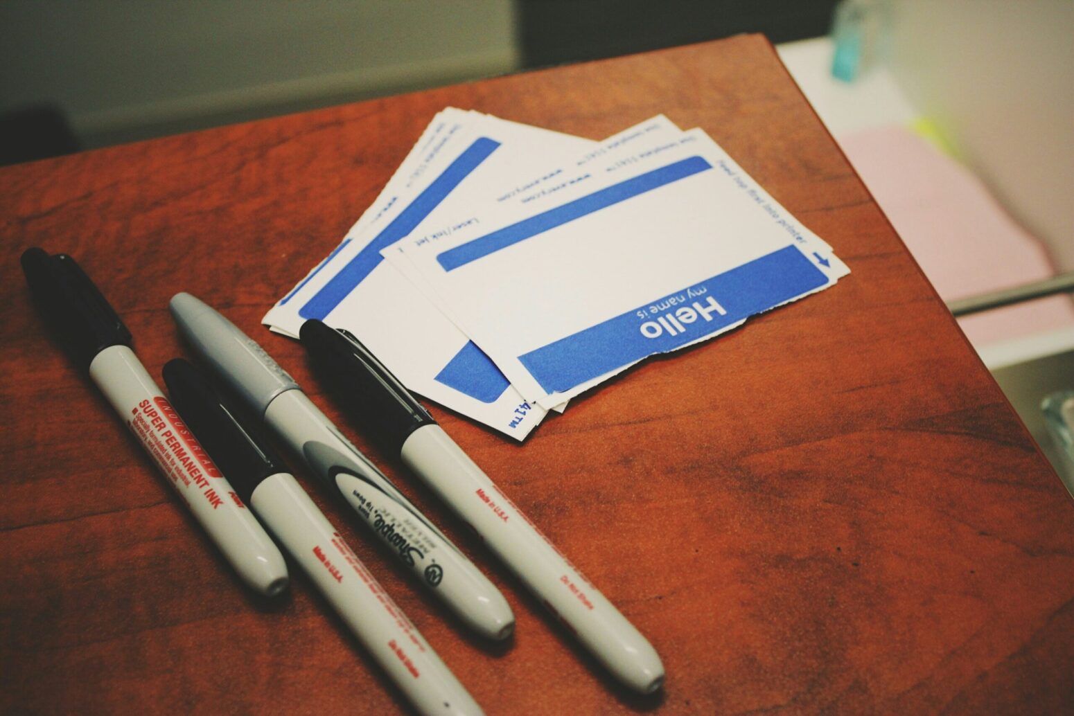 A wooden desk with permanent markers and name tag stickers laying on top.