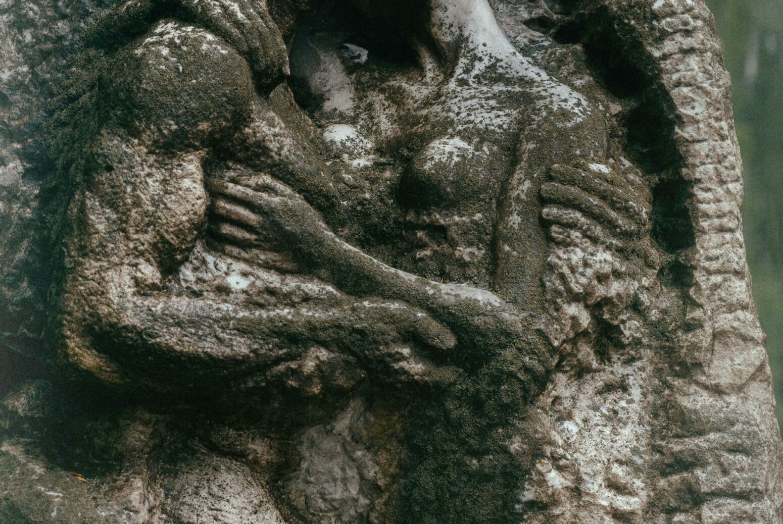 A mossy, stone statue of a man and a woman embracing. The man is very muscular, and he holds the woman's arm with one hand and her waist with the other.