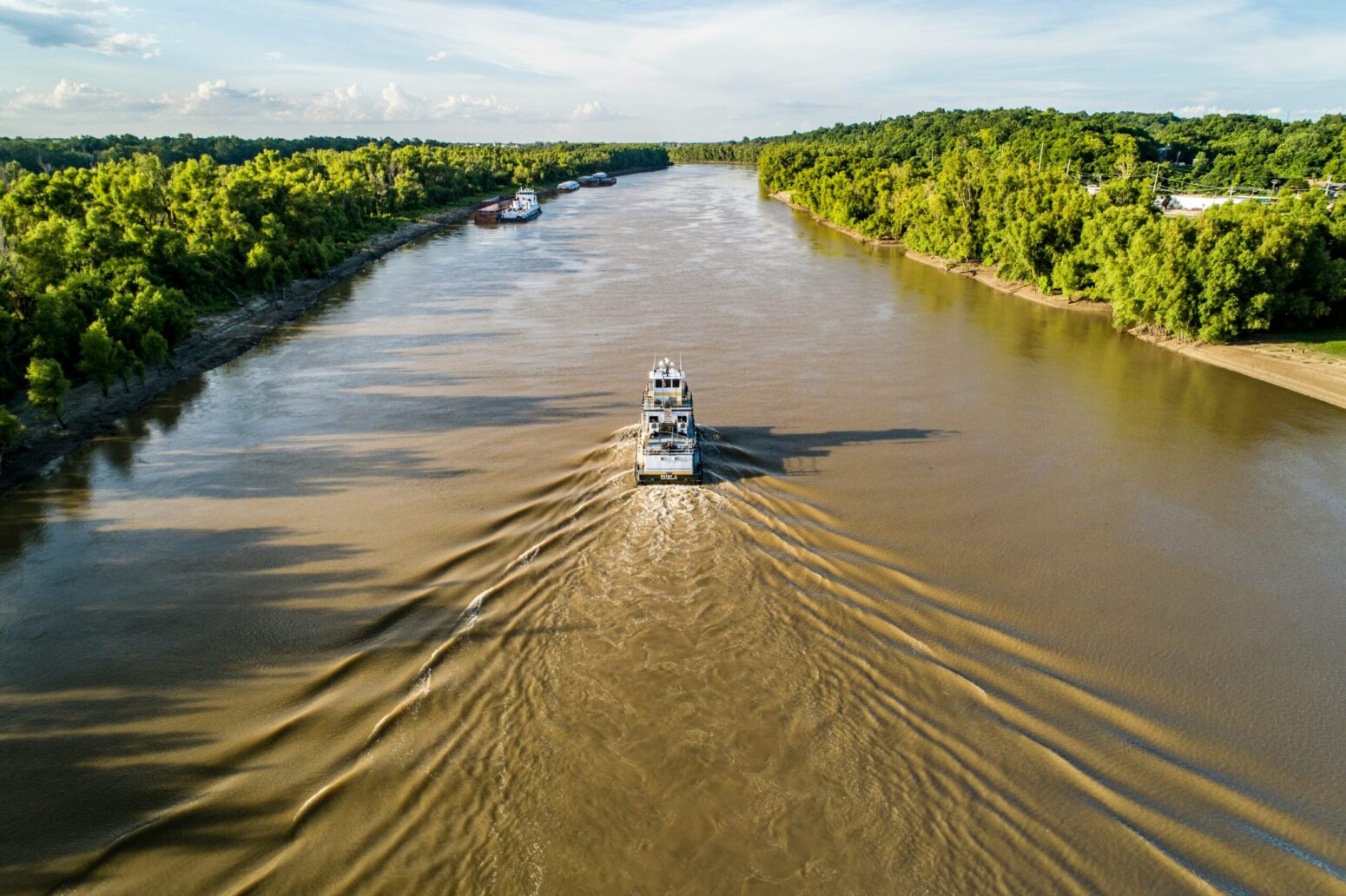 A birds-eye view of a steamboat on the Mississippi River. Forest is on either side of the river.