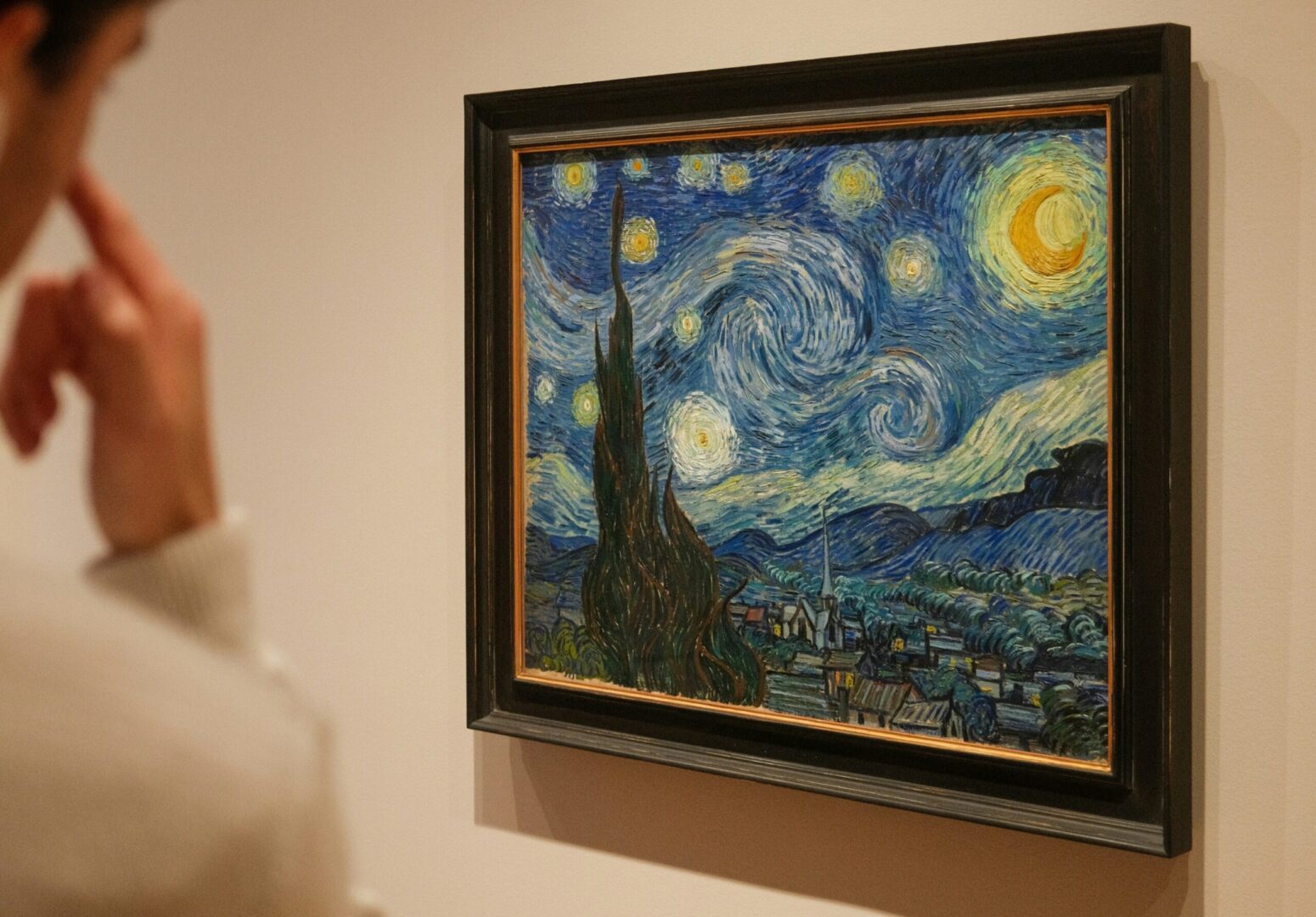 A man in a white shirt looking at "Starry Night" by Vincent van Gogh on a white wall.