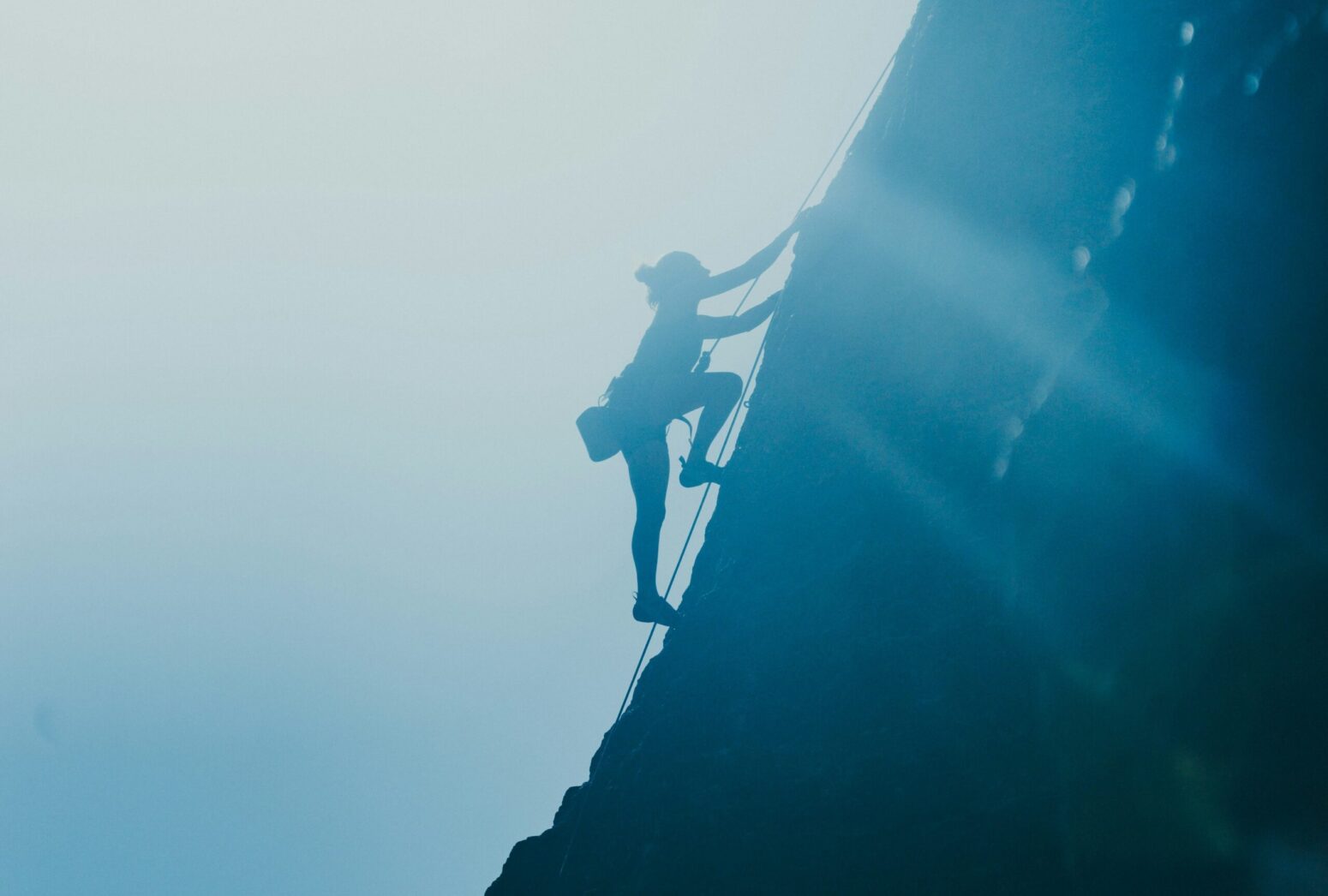 A blue silhouette of a woman climbing up a steep mountain.
