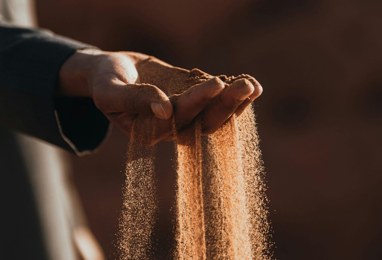 Sand, lit by the sun, falling through a person's fingers