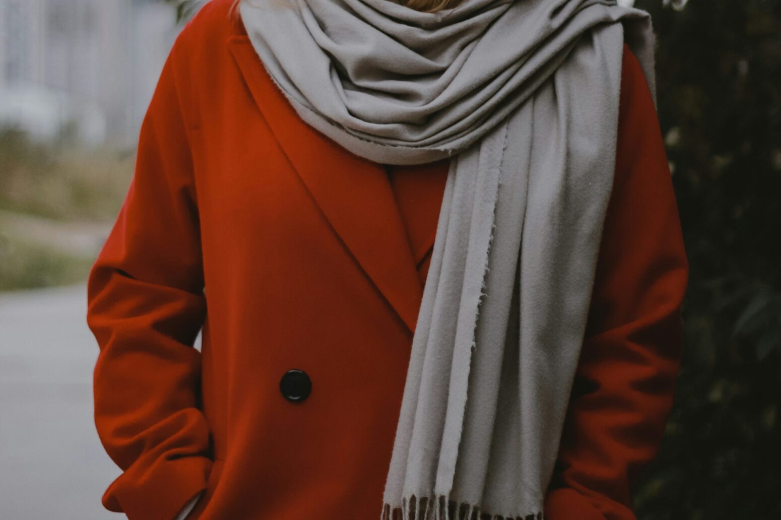 A person in a red coat and a white scarf, with their hands in their pockets. Their head and legs are cut off by the photo. They stand outside.