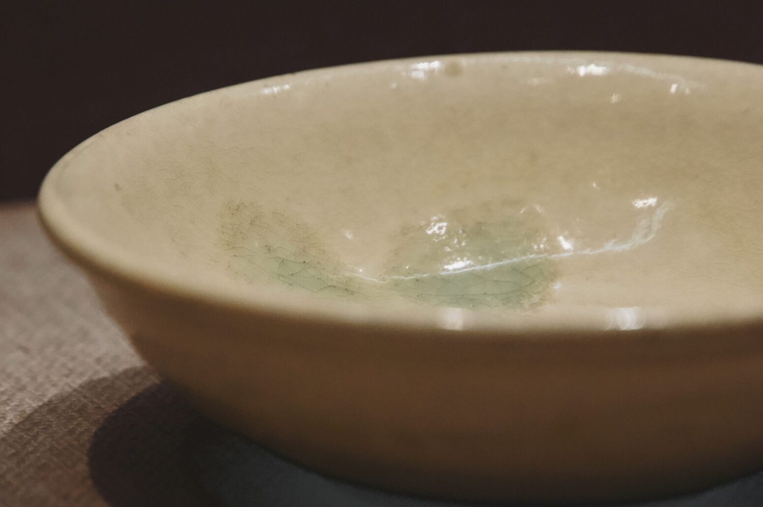 A close-up of an empty, ceramic bowl sitting on a table in a dark room.