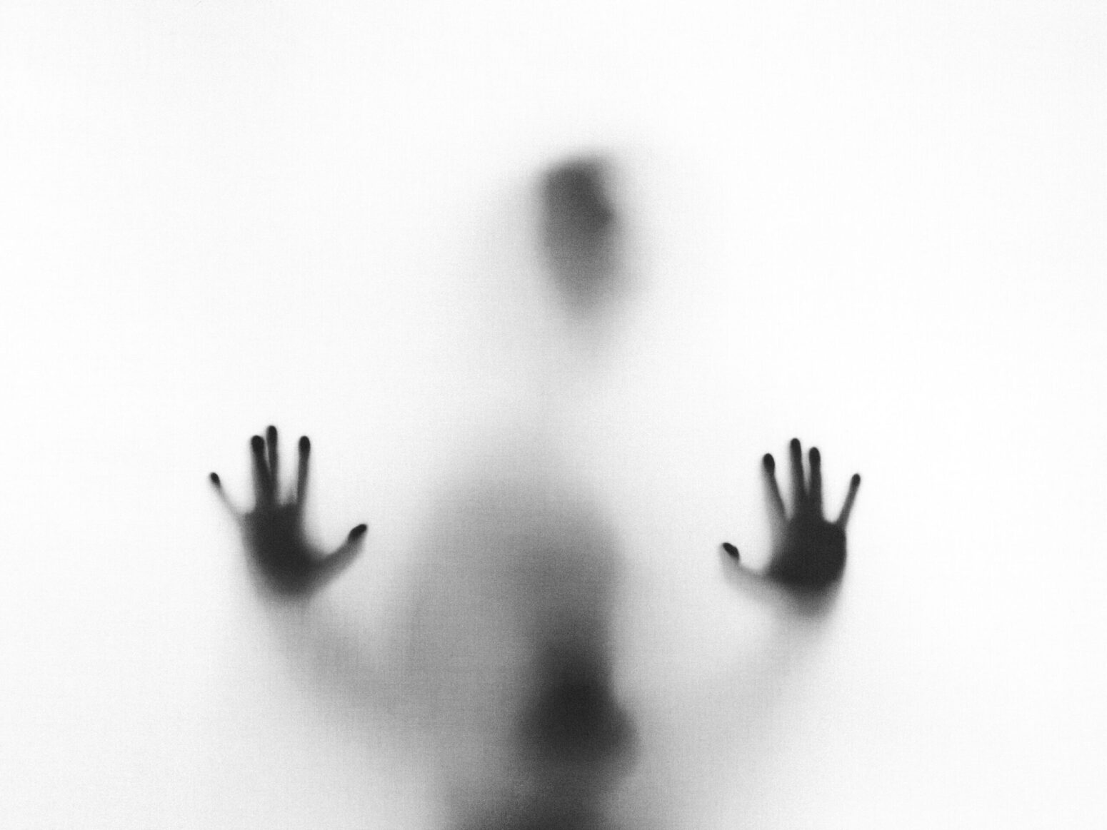 A vague shape of a person behind fogged glass, with the hands and head most recognizable