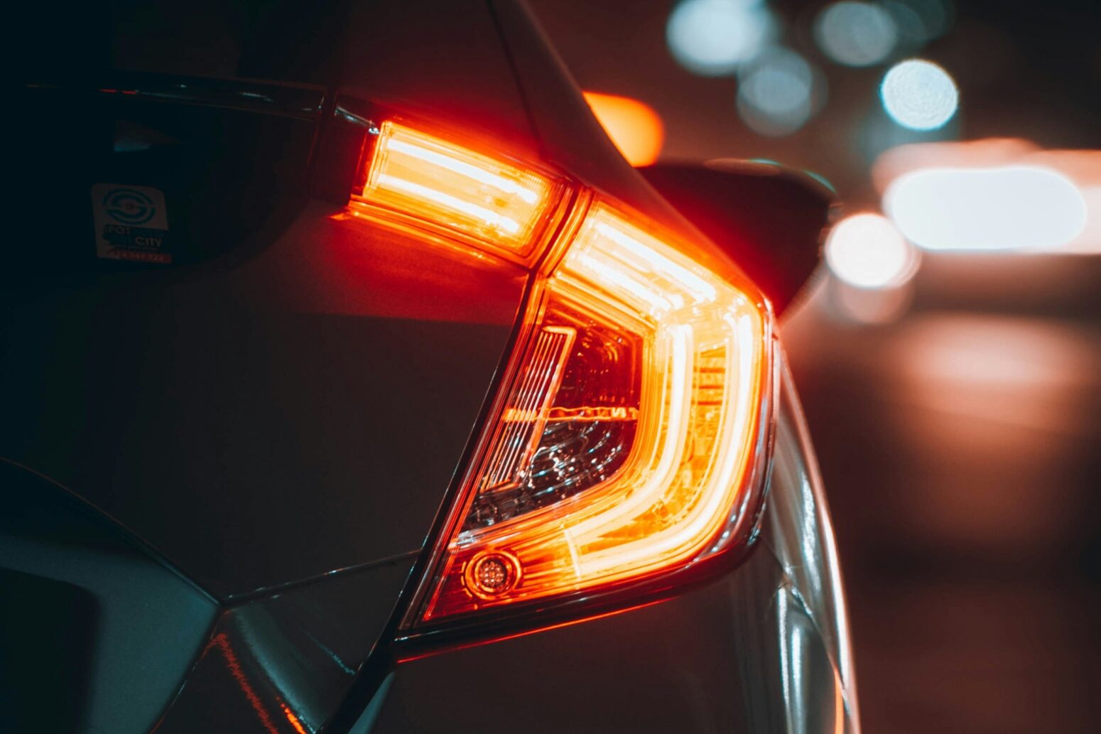 A taillight of a black car in the night. It is lit up with red.