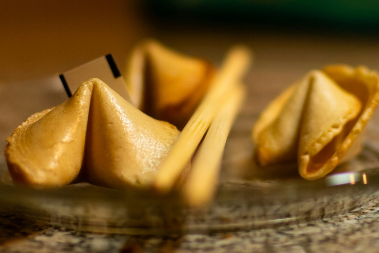 Three fortune cookies lay in a glass dish, with a pair of chopsticks between them.