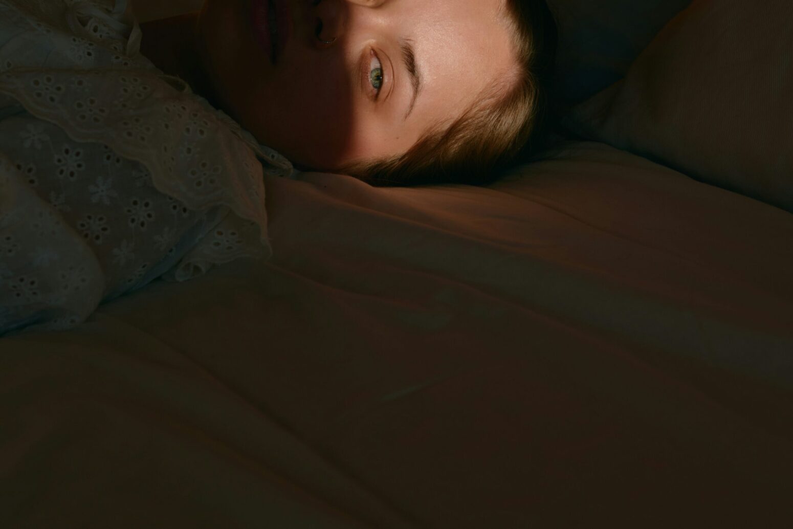 A person laying on their bed in the dark. Only their eyes are illuminated.