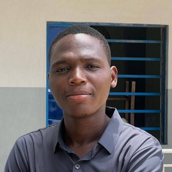 A man with a black buzzcut and brown eyes. He wears a navy, button-up shirt