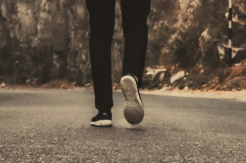 A view from the legs down of someone walking on a road surrounded by cliffs.