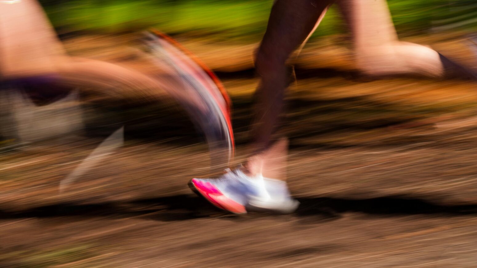 A blurry picture of the legs of two runners. They run on a dirt path and wear white, blue, and neon-orange shoes.