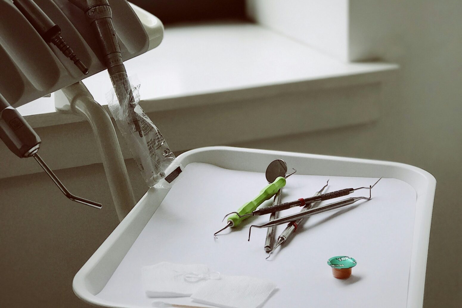 A dentist's office, which a small metal table with various dental tools sitting on it and hanging next to it.