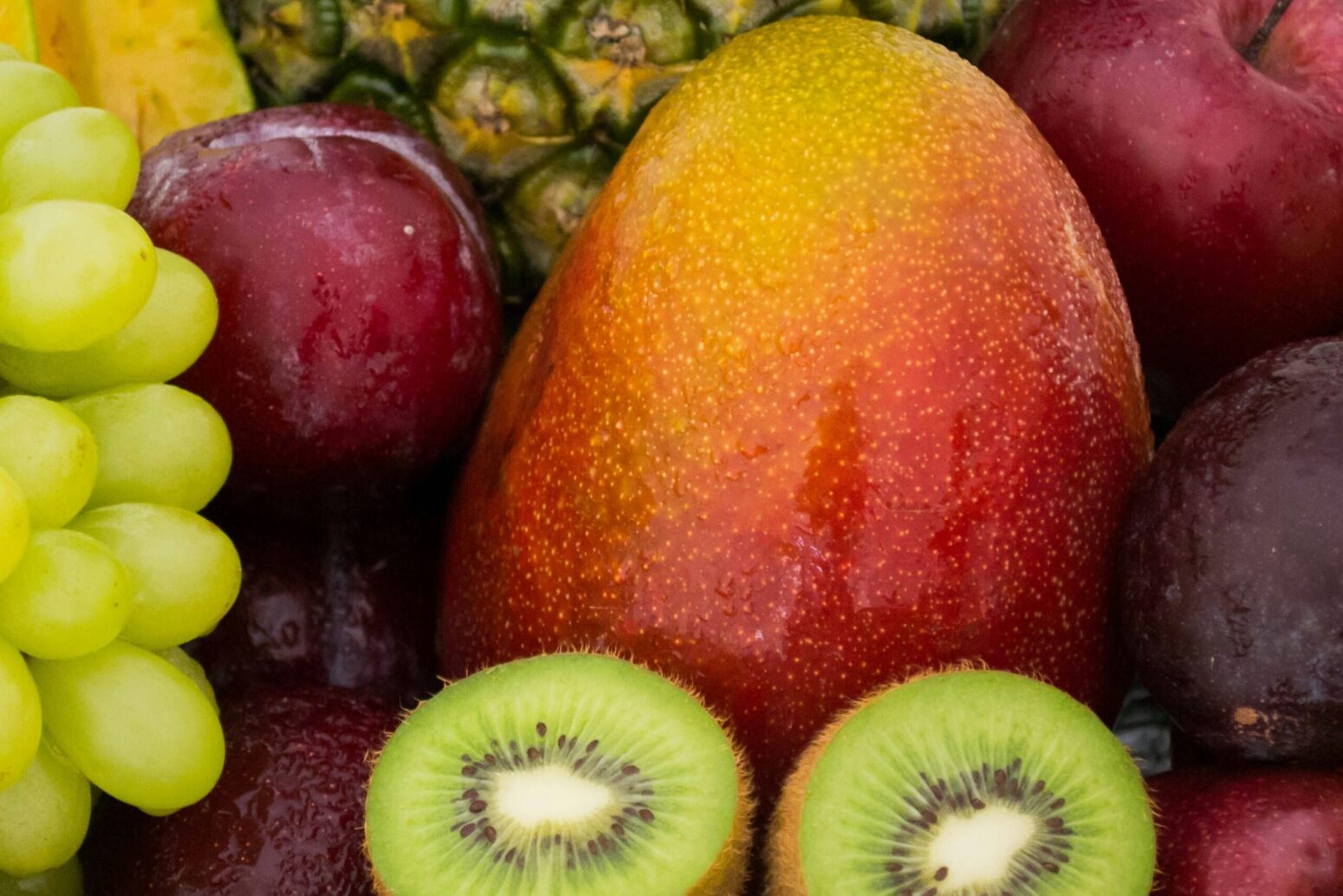 A collection of various fruit. From top left to bottom right, they are starfruit, green grapes, red apple, pineapple, avocado, mango, another red apple, plum, kiwi, and another red apple.