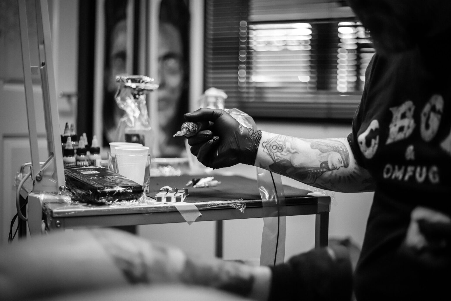 A grayscale photo of a tattoo artist holding a tattoo gun over a work station