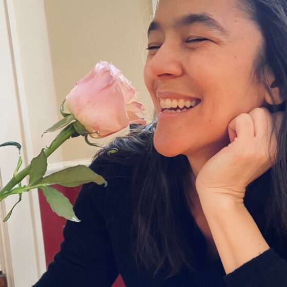 A woman, smelling a rose, smiling with eyes closed.