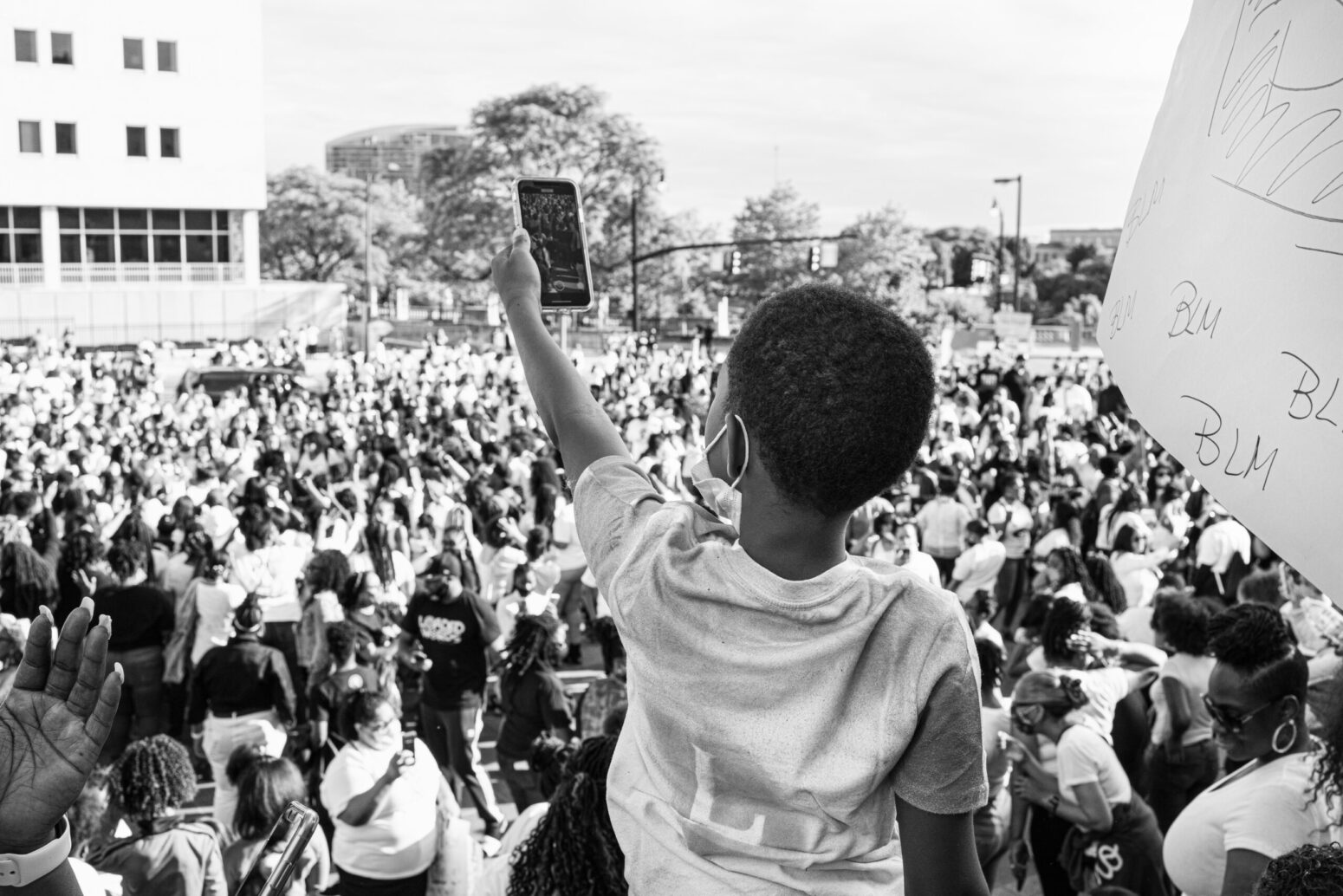 A black-and-white photo of a child taking a photo of a sea of Black Lives Matter protesters