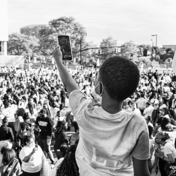 A black-and-white photo of a child taking a photo of a sea of Black Lives Matter protesters