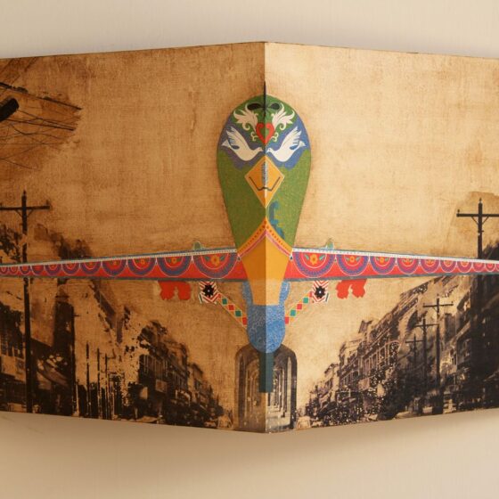 A corner of birch plywood hung up on a wall. Photo-transferred onto the plywood is a colorful plane flying through a black and white city, crowded with buildings and powerlines.