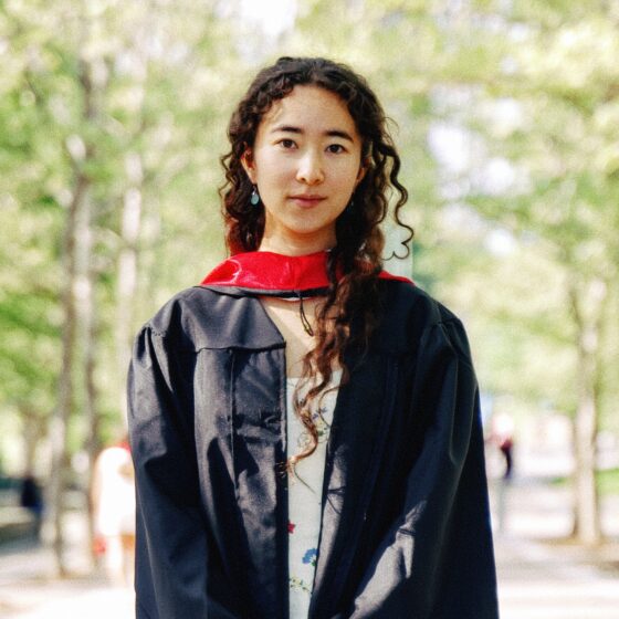 Hana Widerman stands in her ceremonial graduation garb amidst a naturalistic campus setting