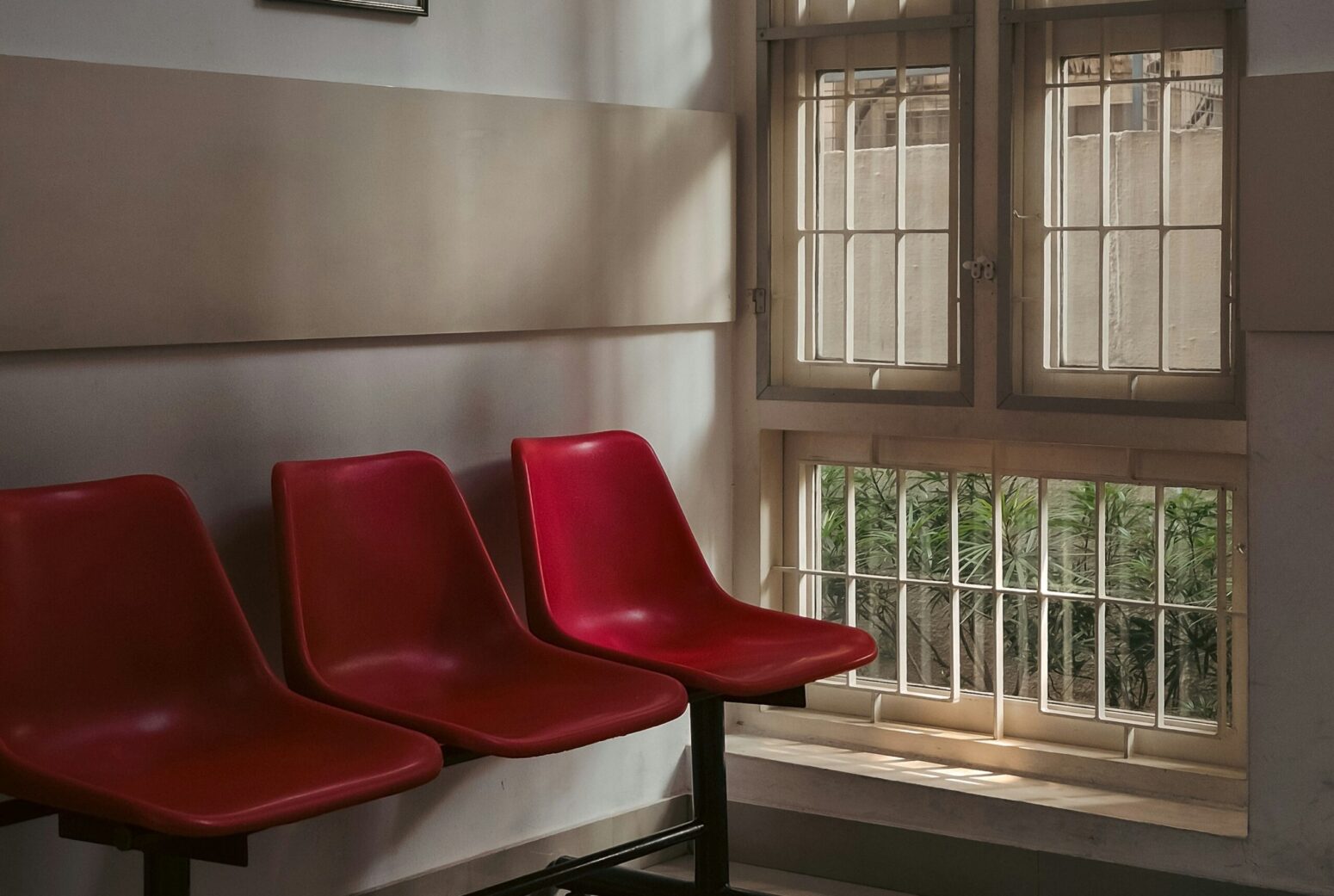 A dimly-lit waiting room, with red chair, white walls, and old windows.