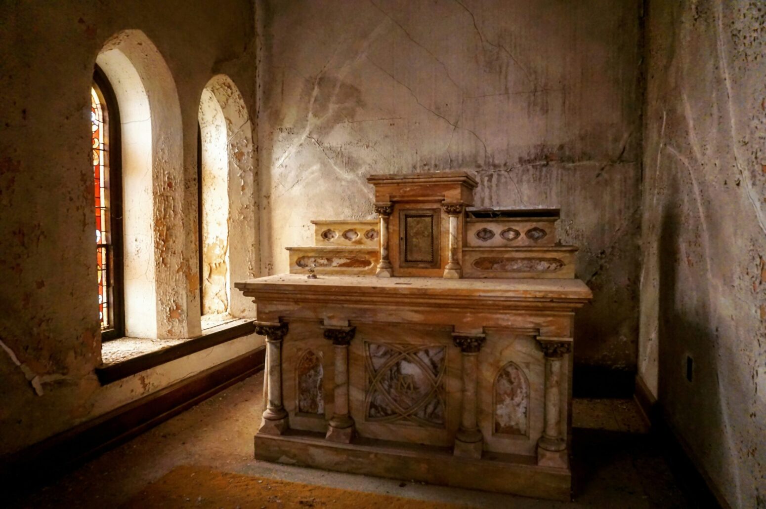 A brown marble altar in a room lit by two stained-glass windows.