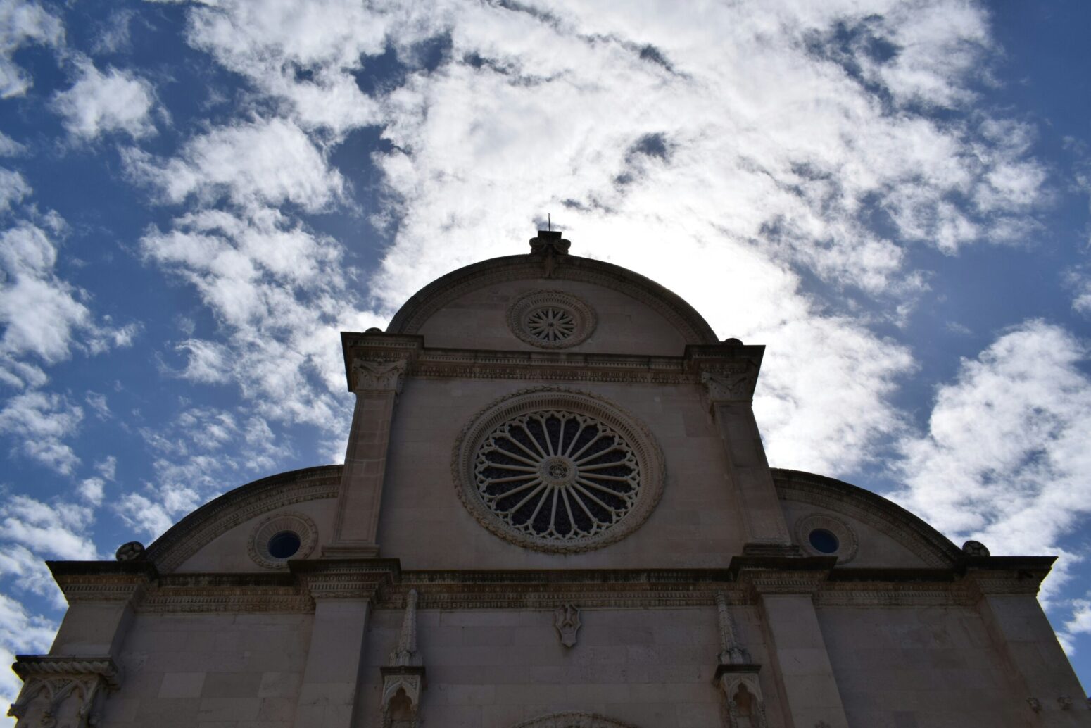 A stone cathedral, silhouetted against a bright, blue, cloudy sky