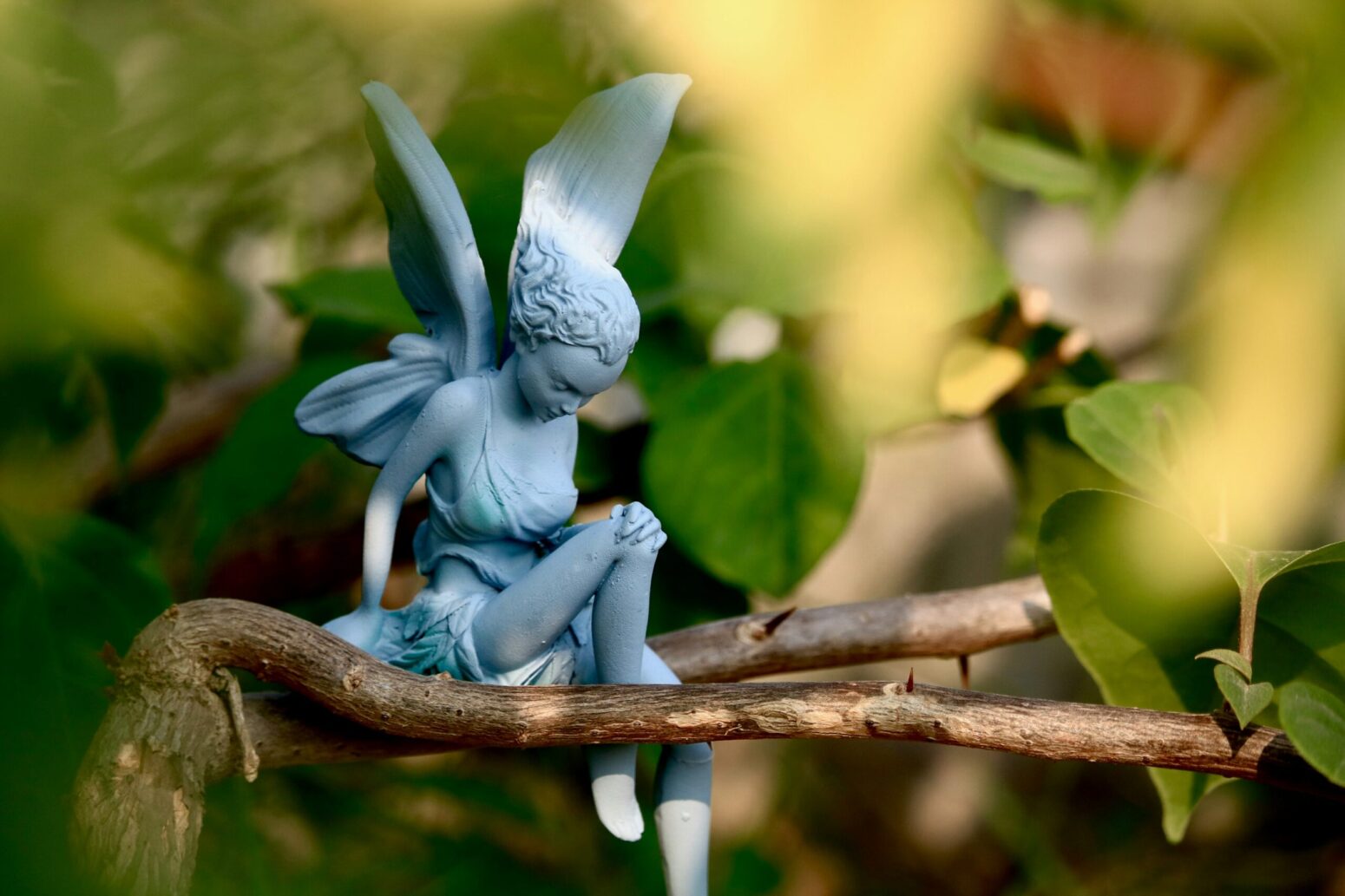 A small statuette of a fairy kneeling on a tree branch.