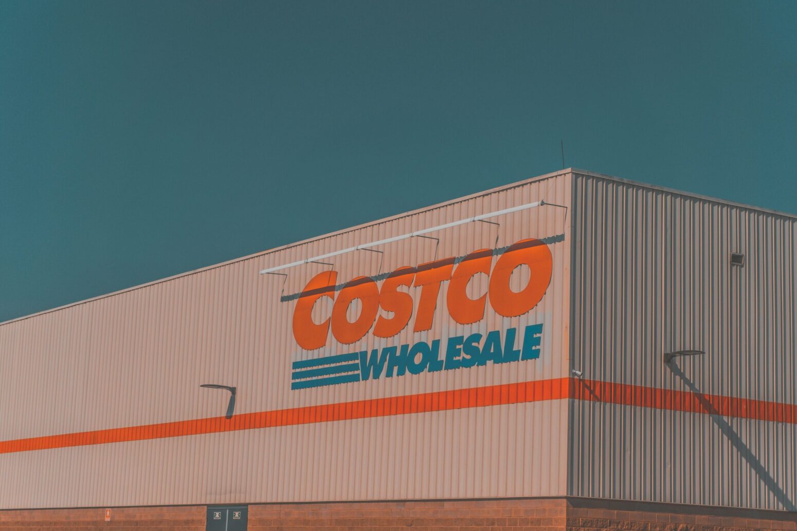 The outside of a Costco. A gray building with a red-and-blue sign that reads "Costco Wholesale"