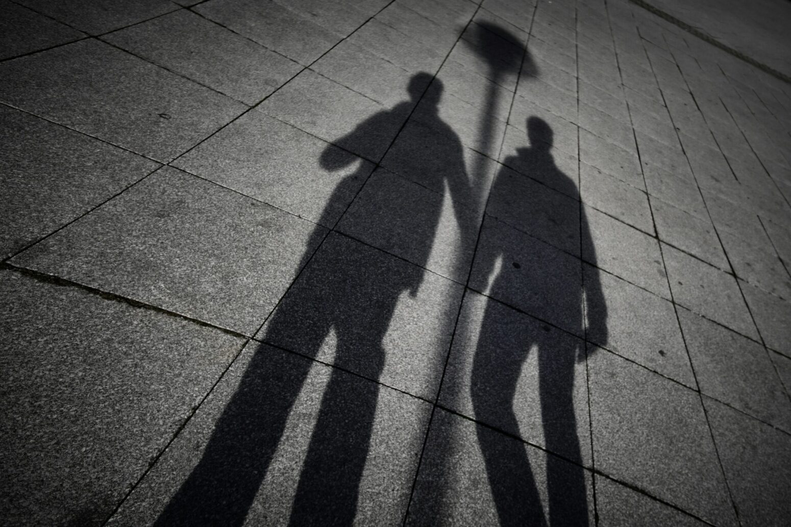 The shadow of two men holding hands on the concrete ground
