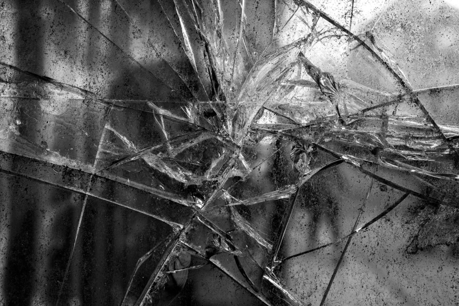 A grayscale, close-up photo of a cracked, blurry window pane