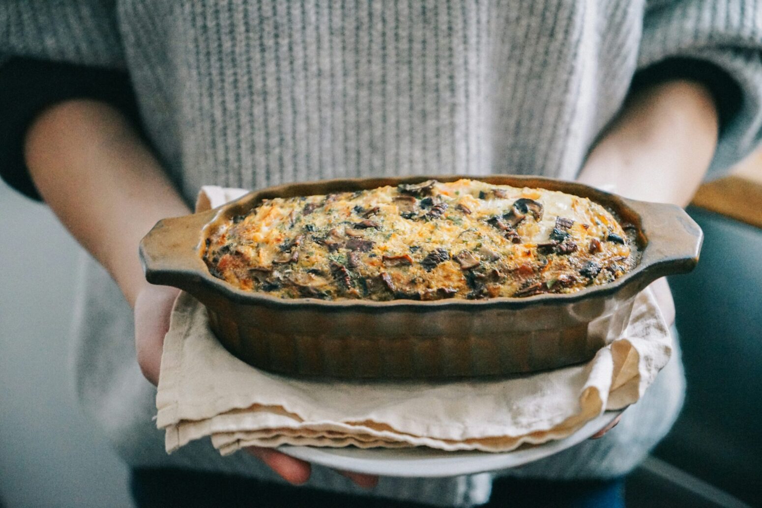 A container of casserole being held by a person wearing a gray sweater