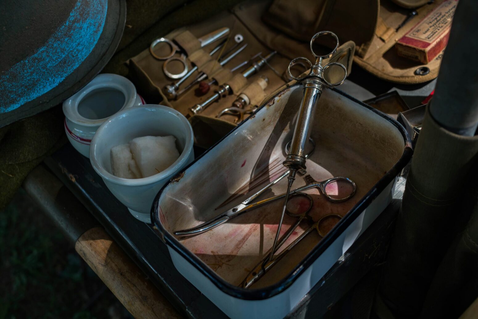 Old-fashioned surgical tools laid out by a bedside, including a stainless-steel syringe, blood-stained scissors, and a wet cloth.