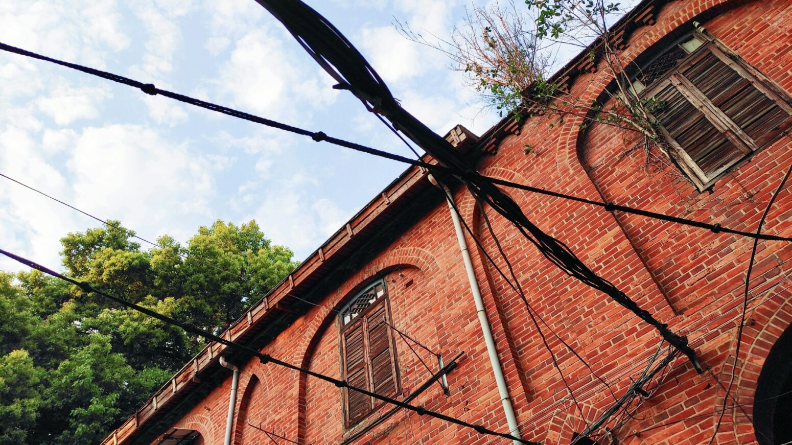An old, run-down, brick building with wooden shutters and electrical wires running to and from it