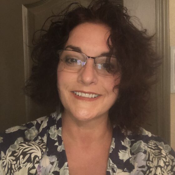 Nicole Brogdon, a white woman with a curly bob and glasses, smiles.