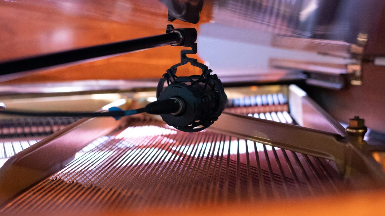 A black metallic microphone under the lid of a grand piano, with threads and other interior workings of the piano visible