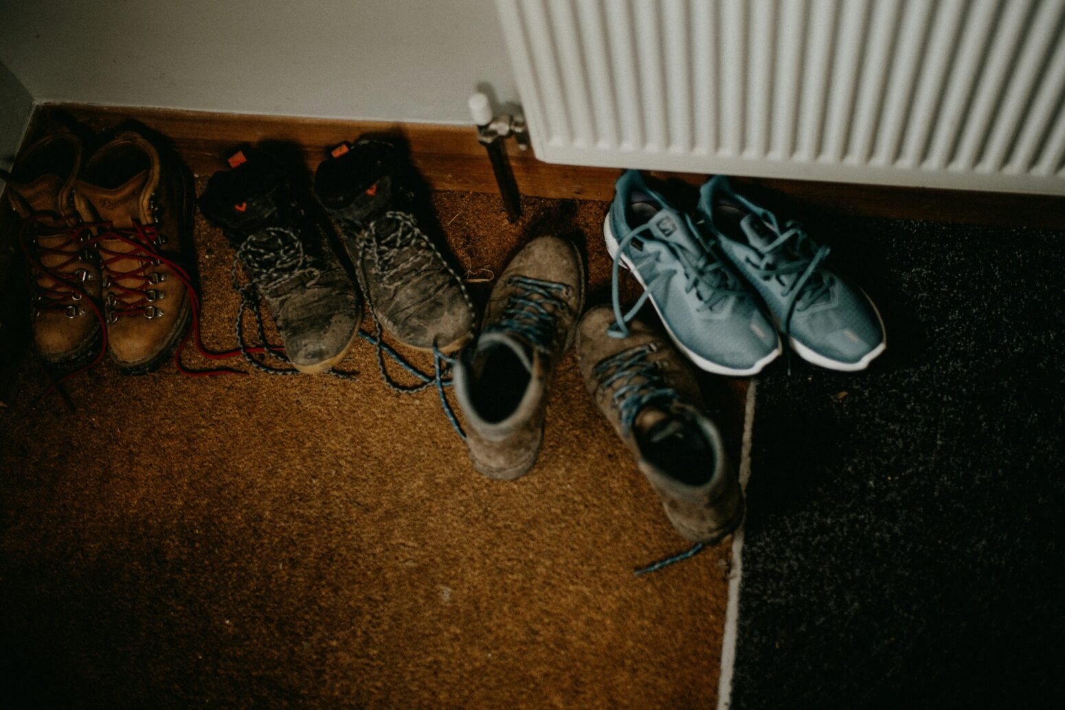 Four pairs of shoes, three brown and one blue, on the floor near a white radiator
