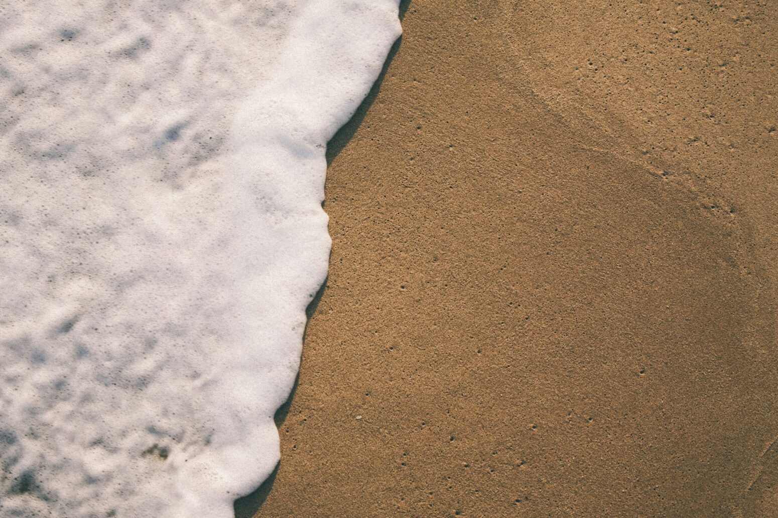 A foamy wave washes over a smooth, sandy beach.