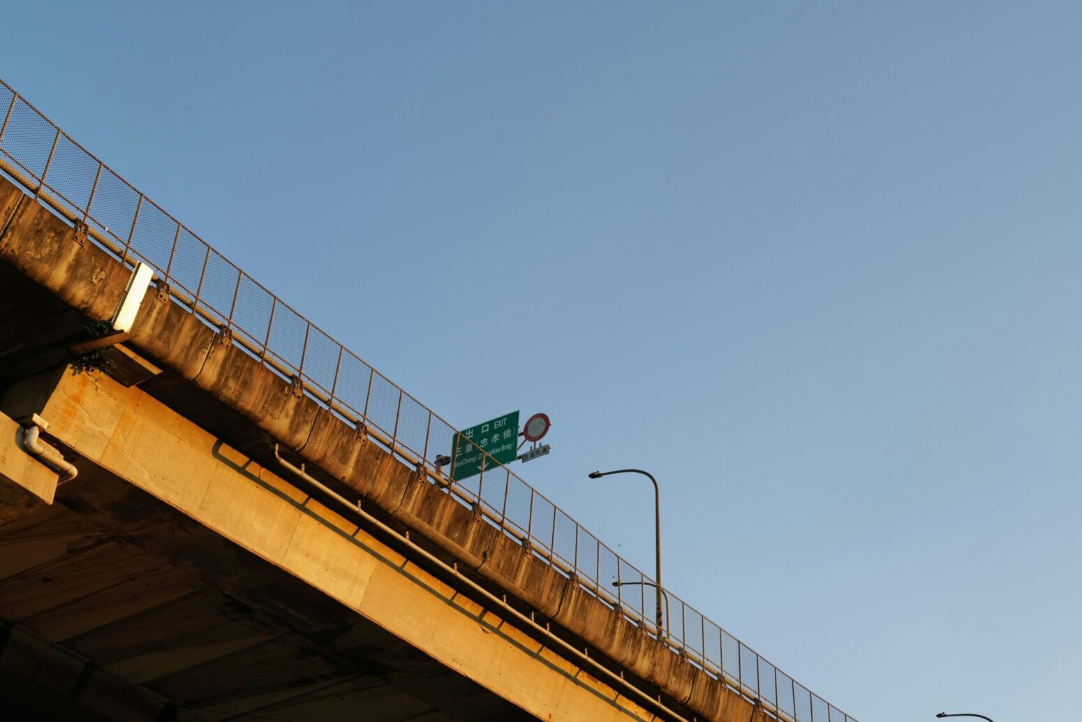 A concrete highway overpass from an angle, with blue sky and a green traffic sign above