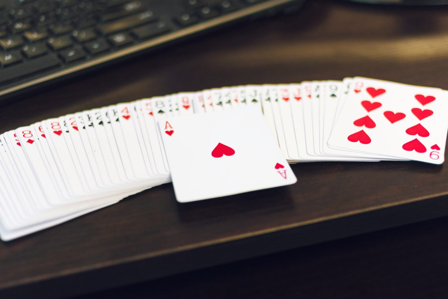 Playing cards fanned out on a brown table (with a computer keyboard in the background). The Ace of Hearts is on top of the cards, prominently
