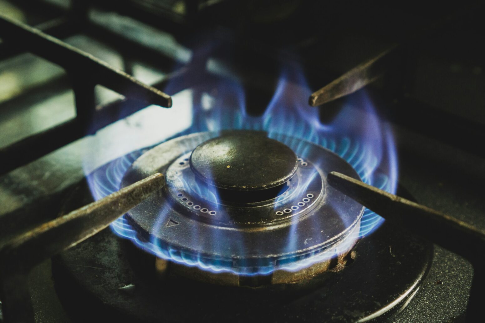 Close-up image of a gas burner on a stovetop with blue flames lit.