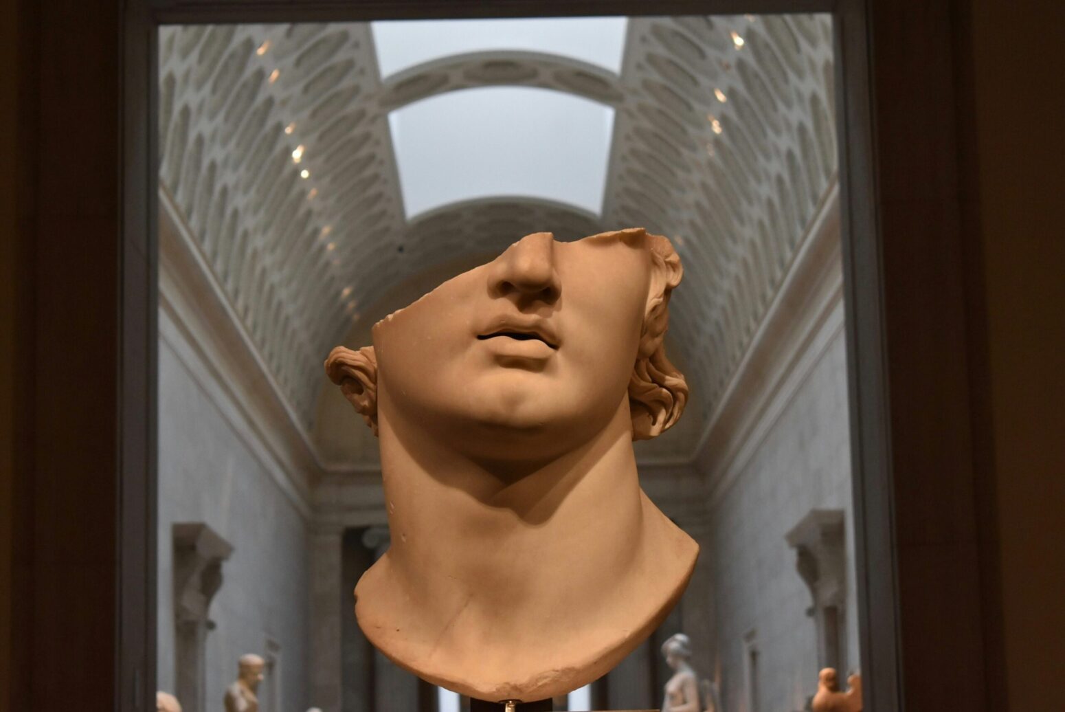 Fragment of a classical statue: the bottom half of a face and neck, framed in the arch of a museum hallway.