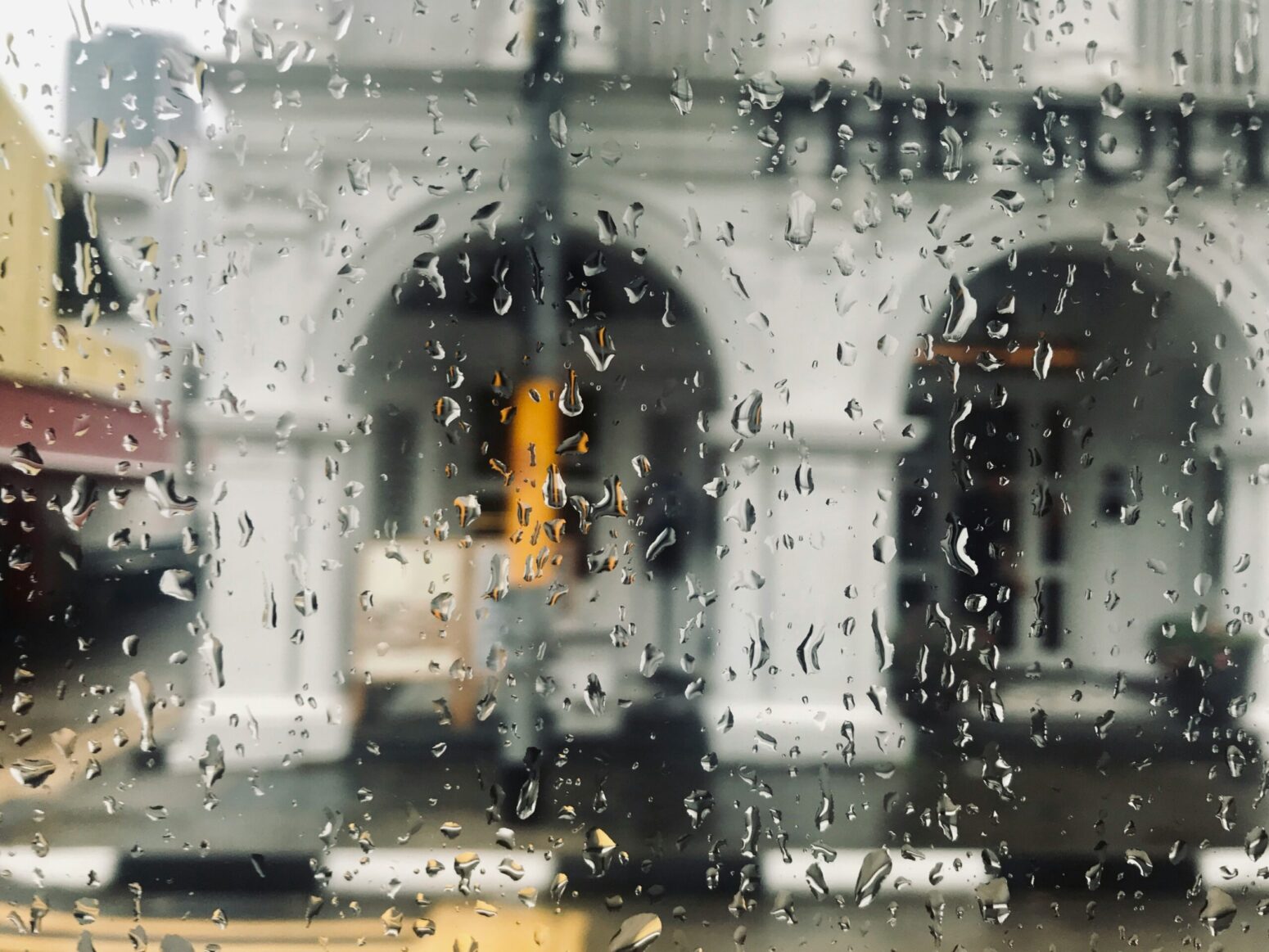 Closeup of rain drops on a window, with the outdoor scene of a stone building with arches, out of focus