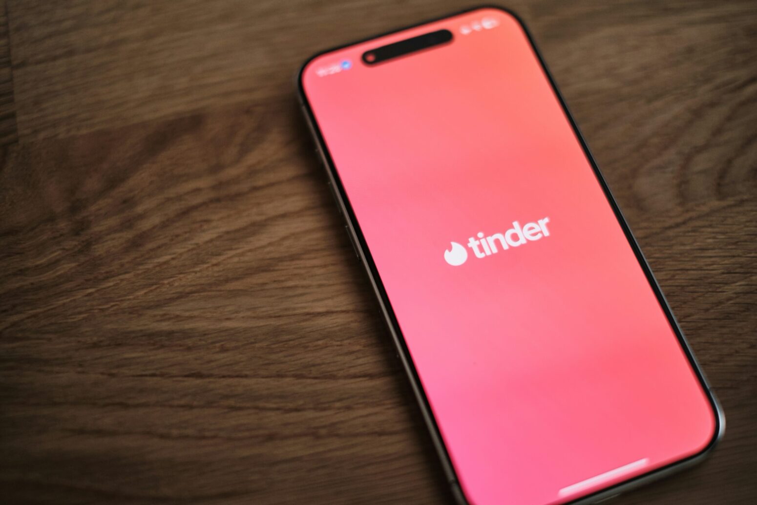 This photograph shows a phone on the wooden surface, with the Tinder app being open on the device.