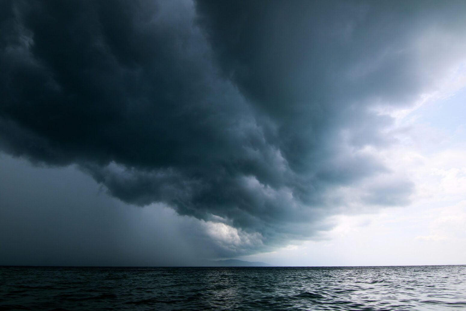 This photograph shows an ocean with a dark gray cloud in the sky, presumably bad weather incoming.