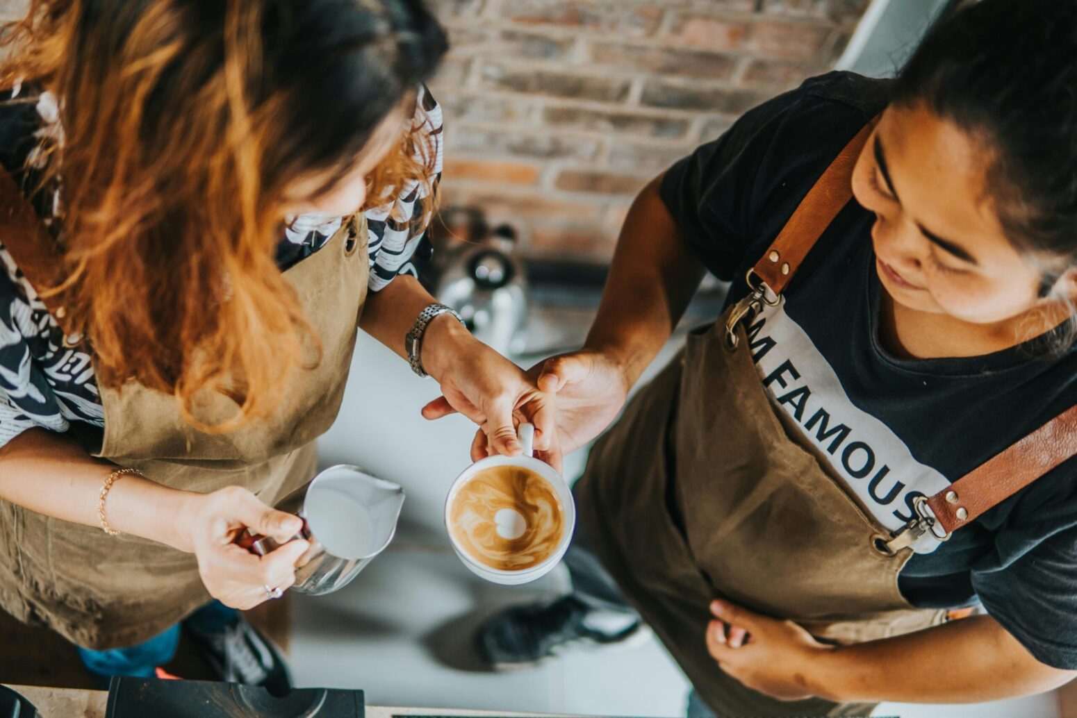 Two hands touch each other: one a barista's holding a coffee, the other a customer's.